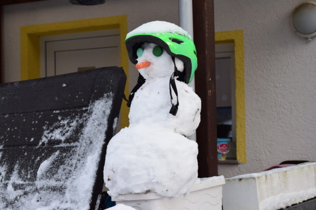 Schneemann mit grünem Helm, grünen Augen und einer Möhre als Nase