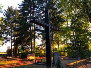 großes schwarzes Holzkreuz auf einem Friedhof mit großen Bäumen im Sommer