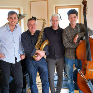 Vier Musiker mit Saxophon und Bass neben einem Klavier
